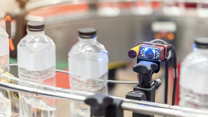 En sensor med et digitalt display kontrollerer flasker på et rullebånd.